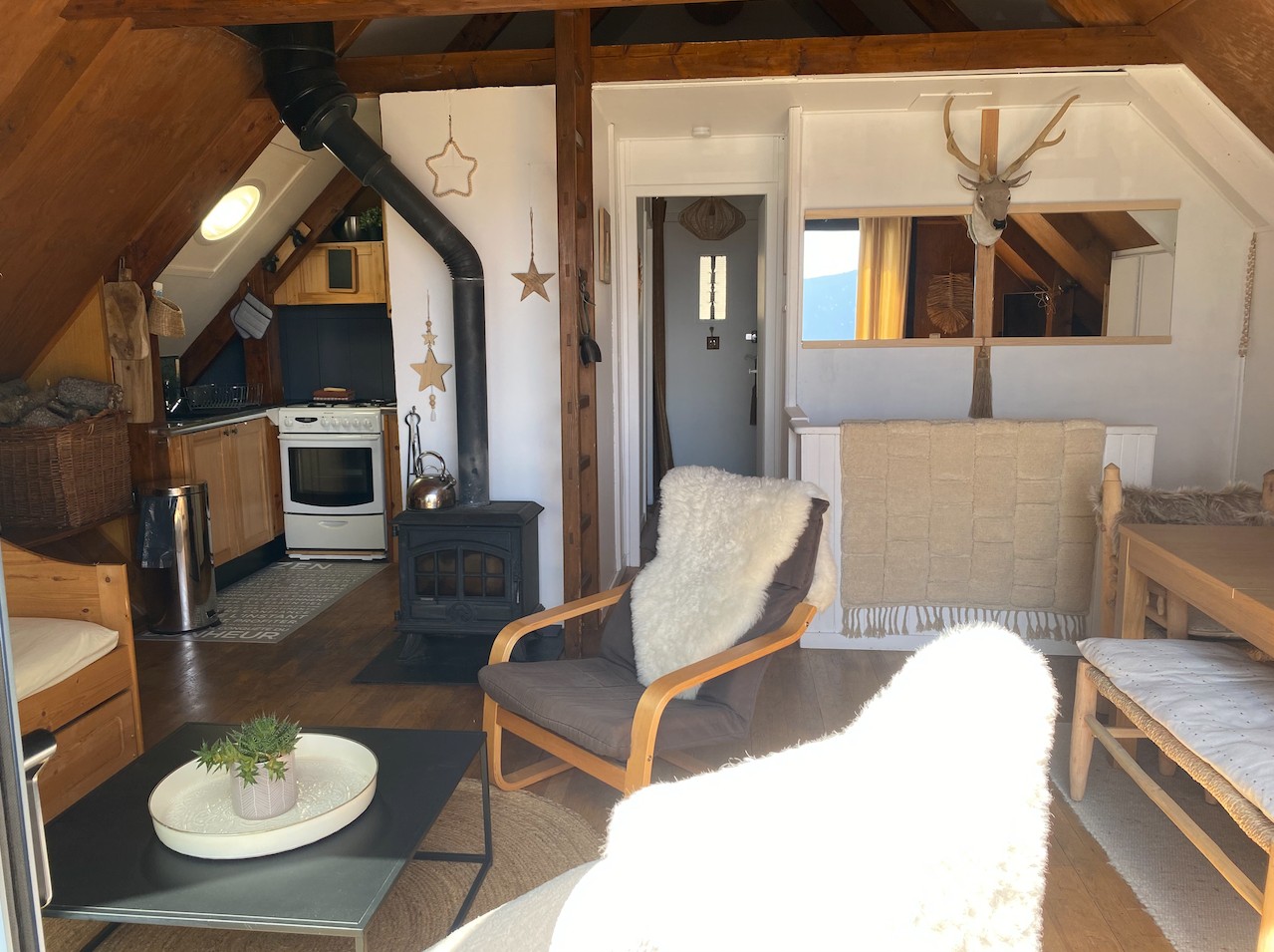 Pièce à vivre de chalet avant rénovation avec cuisine ouverte, poêle, bois foncé et salon limité.